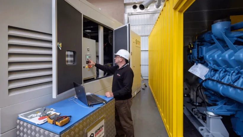 Técnico de Genesal Energy realizando una inspección y ajuste en el panel de control de un grupo electrógeno industrial.